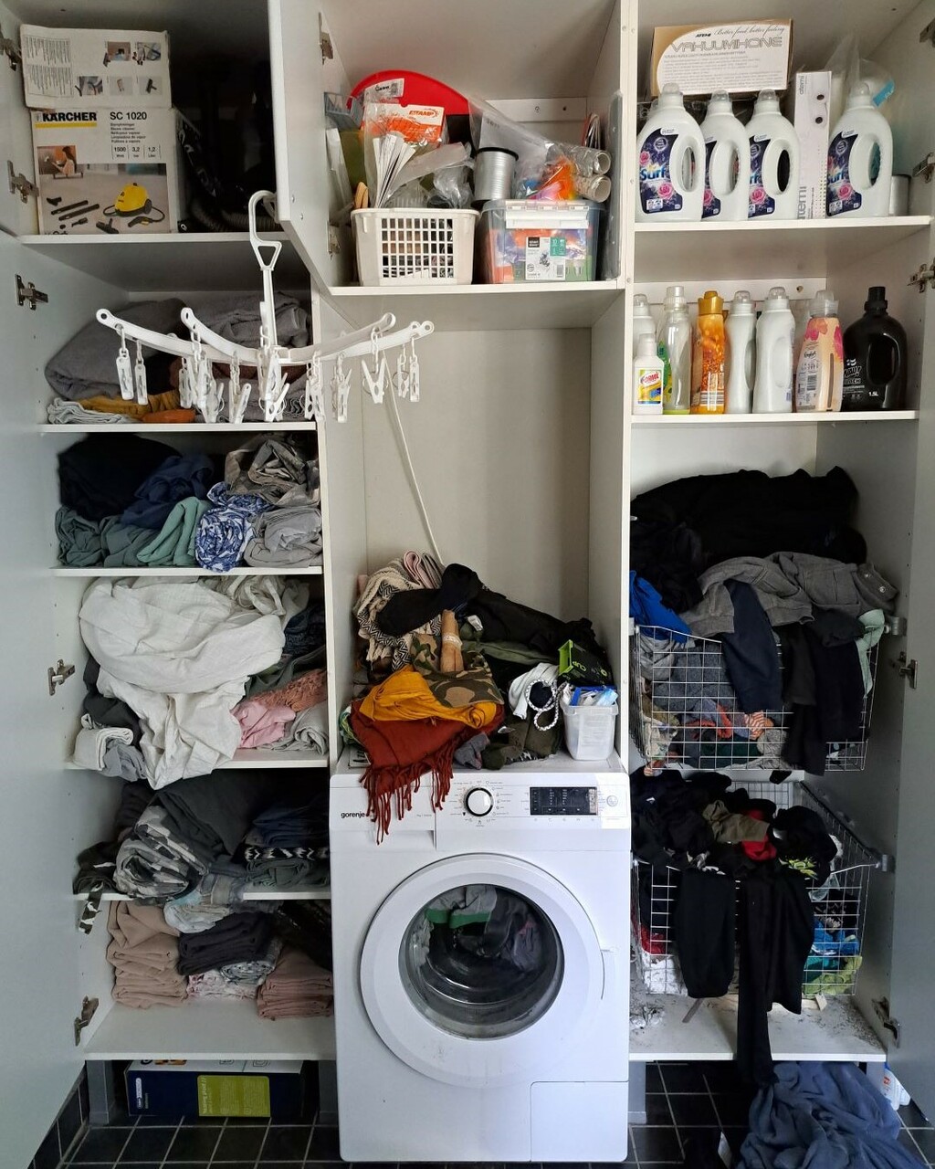 Kodinhoitohuoneen kaapit on sullottu täyteen pyykkejä, pyyhkeitä ja lakanoita. Hyllyt ovat täynnä pesuainepulloja ja pyykinpesukoneen päällä on vaatteita.