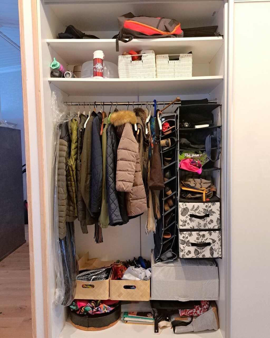 Eteisen tankokaapissa on takkeja, kenkiä ja muuta tavaraa epäkäytännöllisessä järjestyksessä. Tavaroita on laitettu erinäköisiin koreihin ja lokerikoihin.