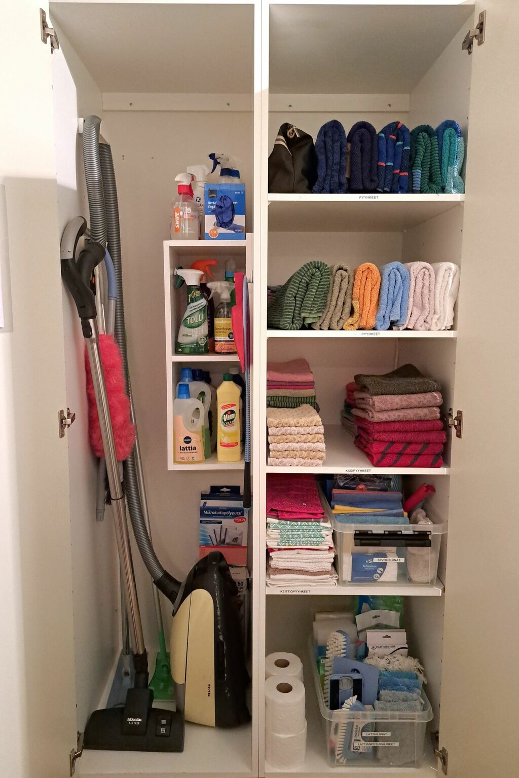 Siivoustarvikkeet on järjestetty kaappiin toimivaan järjestykseen. Kylpypyyhkeet on pystyviikattu hyllylle ja käsipyyhkeet on järjestetty siisteihin pinoihin.